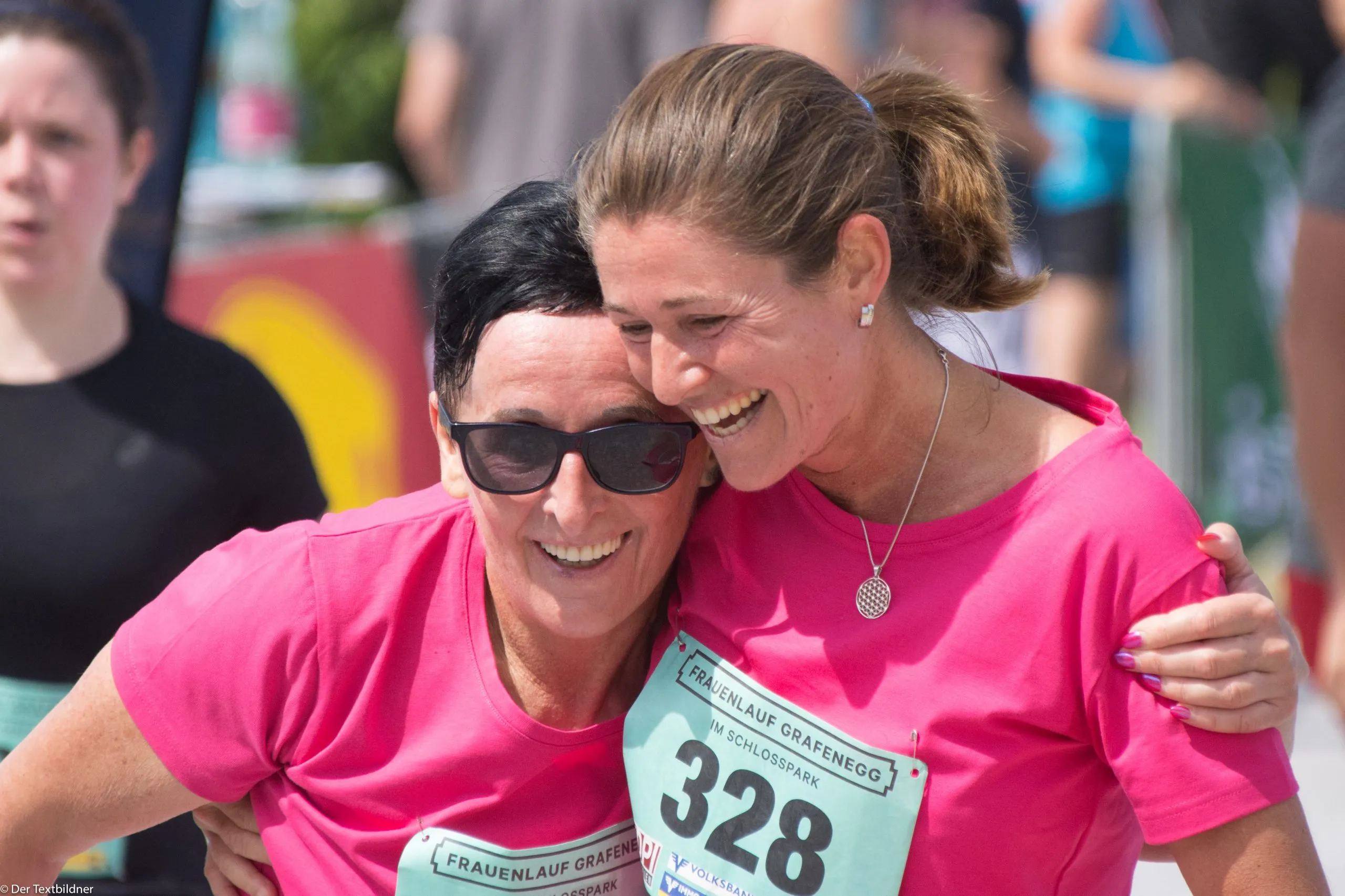 Zwei Läuferinnen in pinken Shirts umarmen sich lachend im Ziel